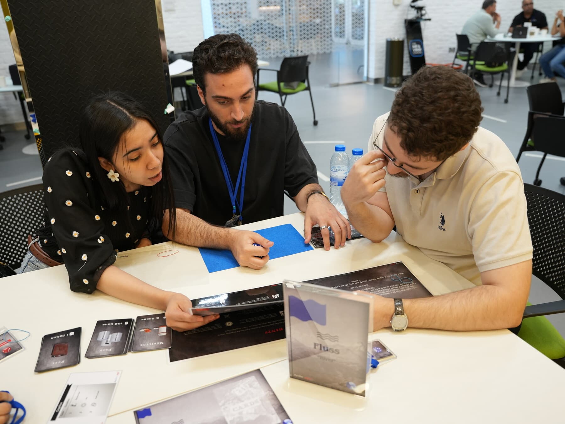Three participants working a Falcon Eye round together, role cards and the Fluss territory card on the table between them.