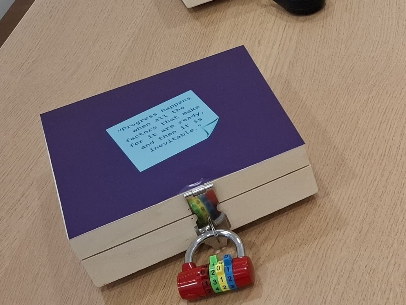 One Flow box close: a quotation card reading “Progress happens when all the factors that make it are ready, and then it is inevitable” above the four-dial combination padlock holding the lid shut.
