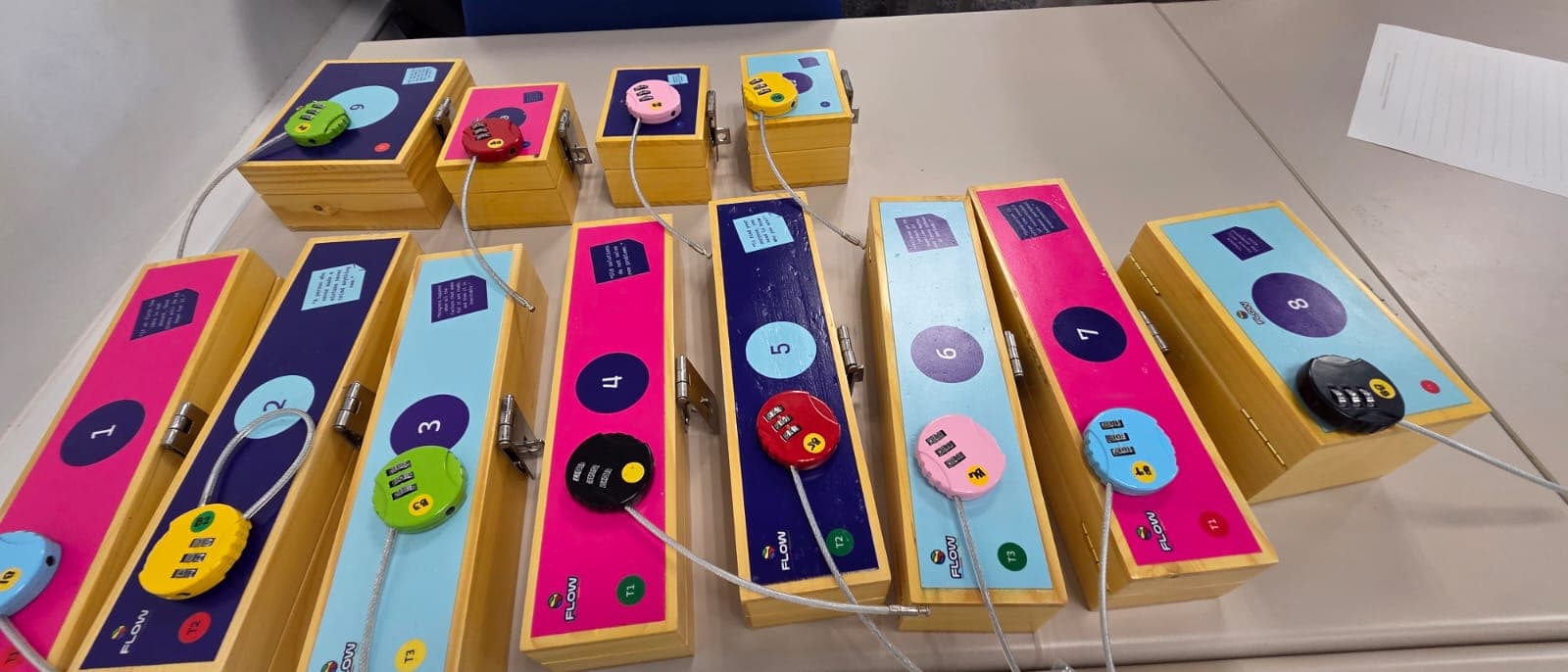 The Flow puzzle set laid out: nine numbered wooden boxes, each printed with a quotation and sealed with its own coloured combination padlock.
