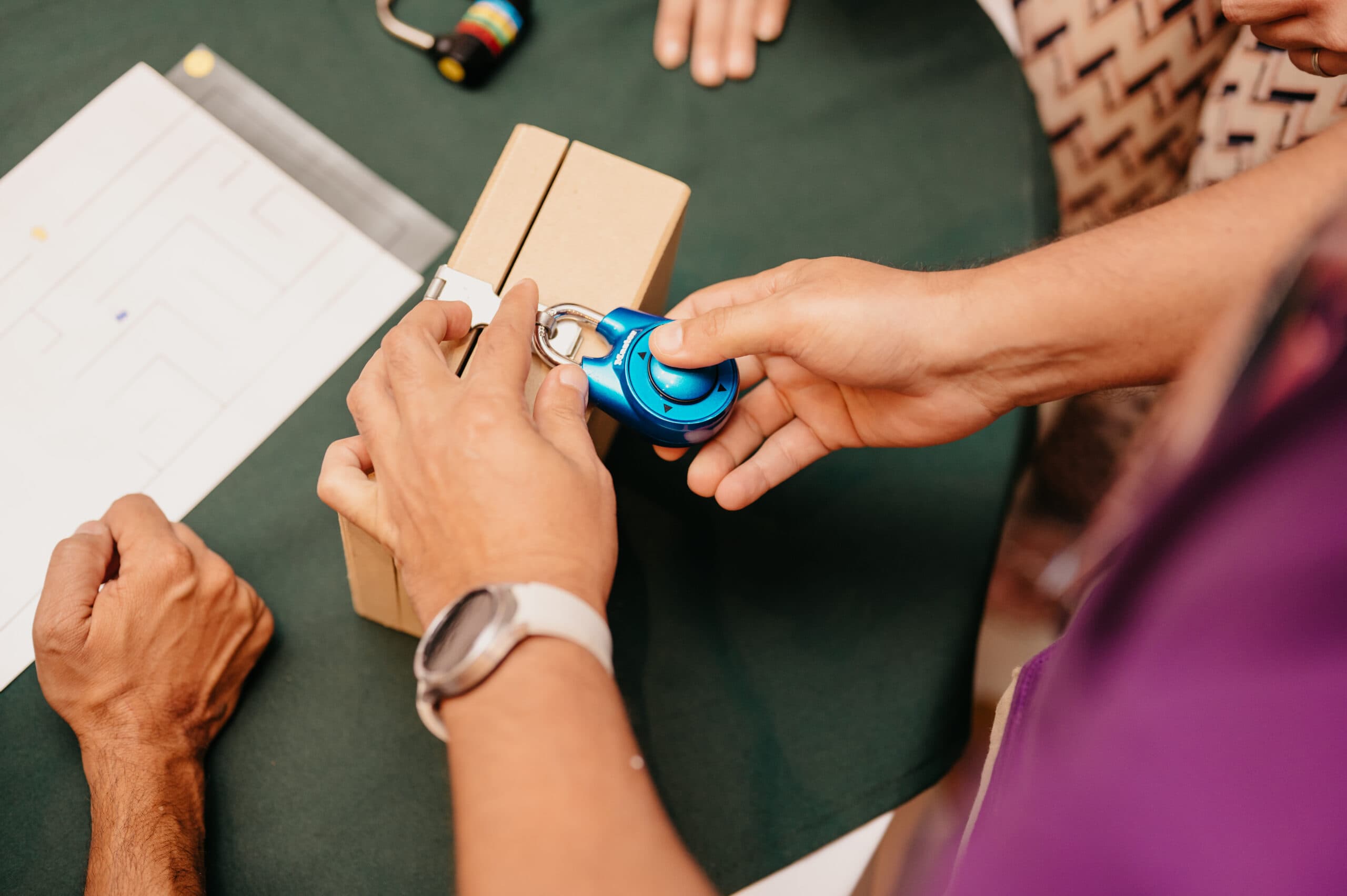 A participant's hands working a coloured padlock on one of the Flow boxes, a puzzle sheet beside it on the table.