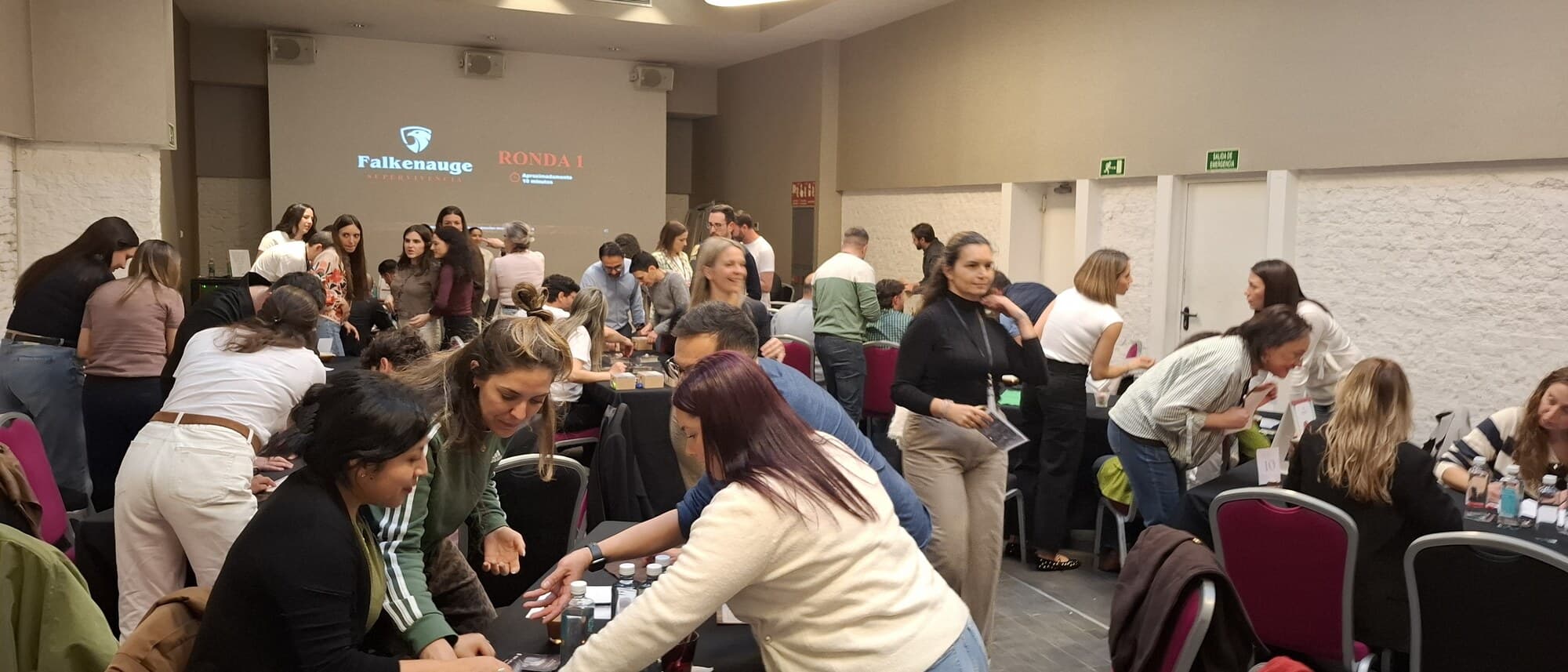 A Falcon Eye round running at conference scale: a dozen tables of participants leaning over their village kits, the round clock projected at the front of the room.